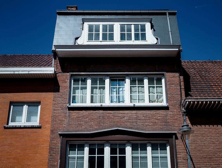 A row of historic red brick terraced houses with ornate architectural details, including bay windows, decorative stonework, and rounded turrets topped with conical roofs, situated on a street with a tree partially visible on the left side. The buildings feature large sash windows and balconies, consistent with traditional Victorian or Edwardian design. This exterior view, captured during daylight, illustrates classic residential architecture typical of the Southall area. Such properties often require careful packing and planning during home relocation or furniture transport, which companies like Man with Van Southall handle efficiently. The image highlights the external environment involved in moving services, emphasizing the importance of securing and protecting furniture and boxes during loading and transport processes, especially when navigating historic or multi-story buildings.